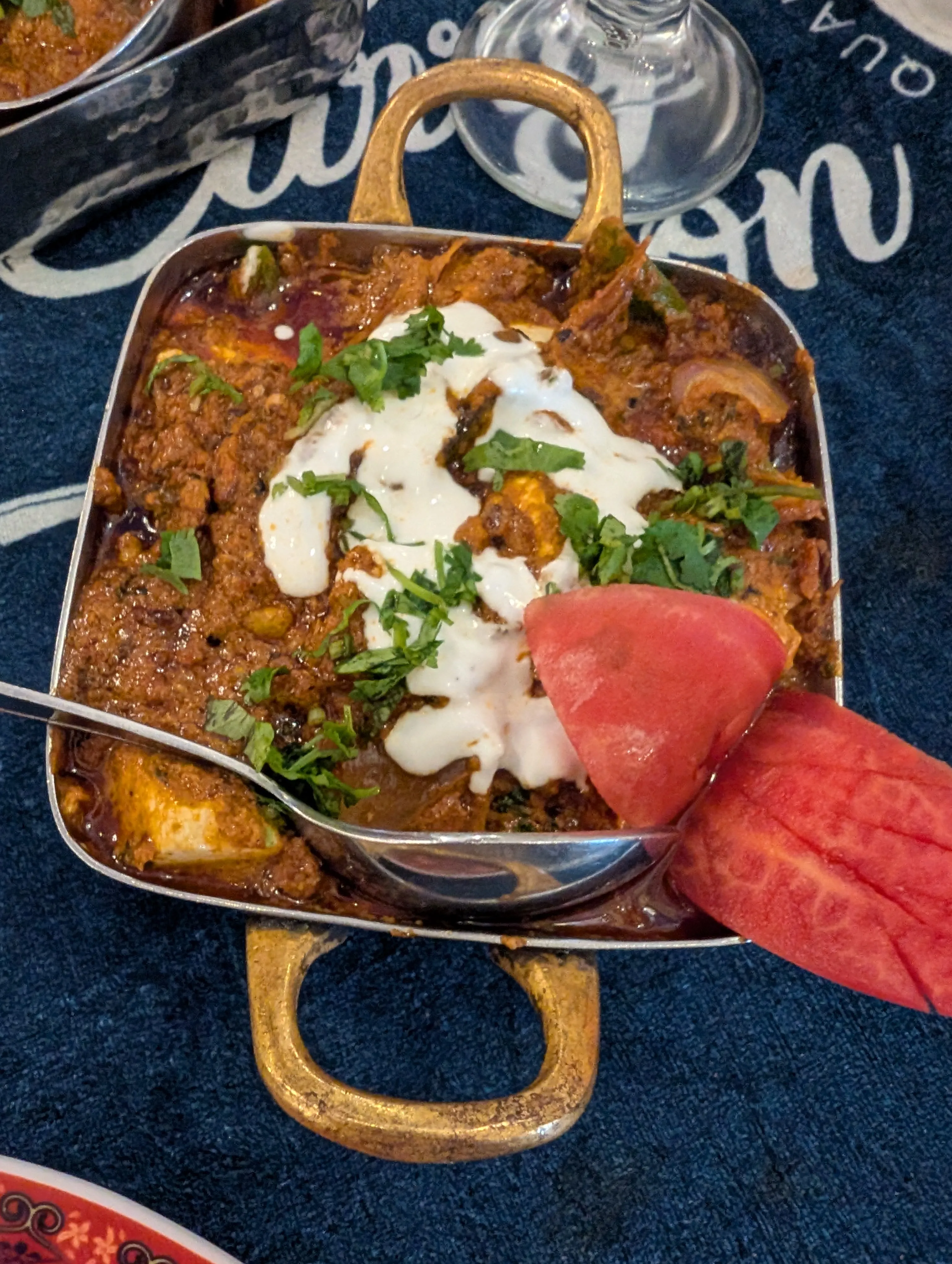 Paneer curry served in a traditional kadai, topped with cream and cilantro.